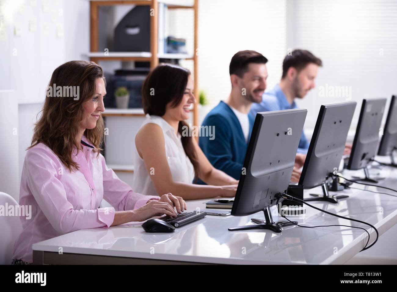 Smiling Young Business People Sitting In A Row Using Computer Stock Photo