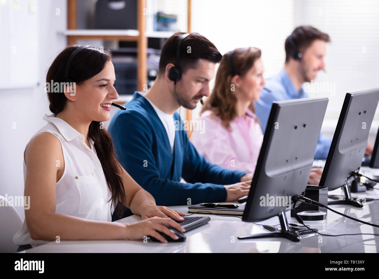 Happy Young Customer Service Executives Using Earphones Working In Call Center Stock Photo