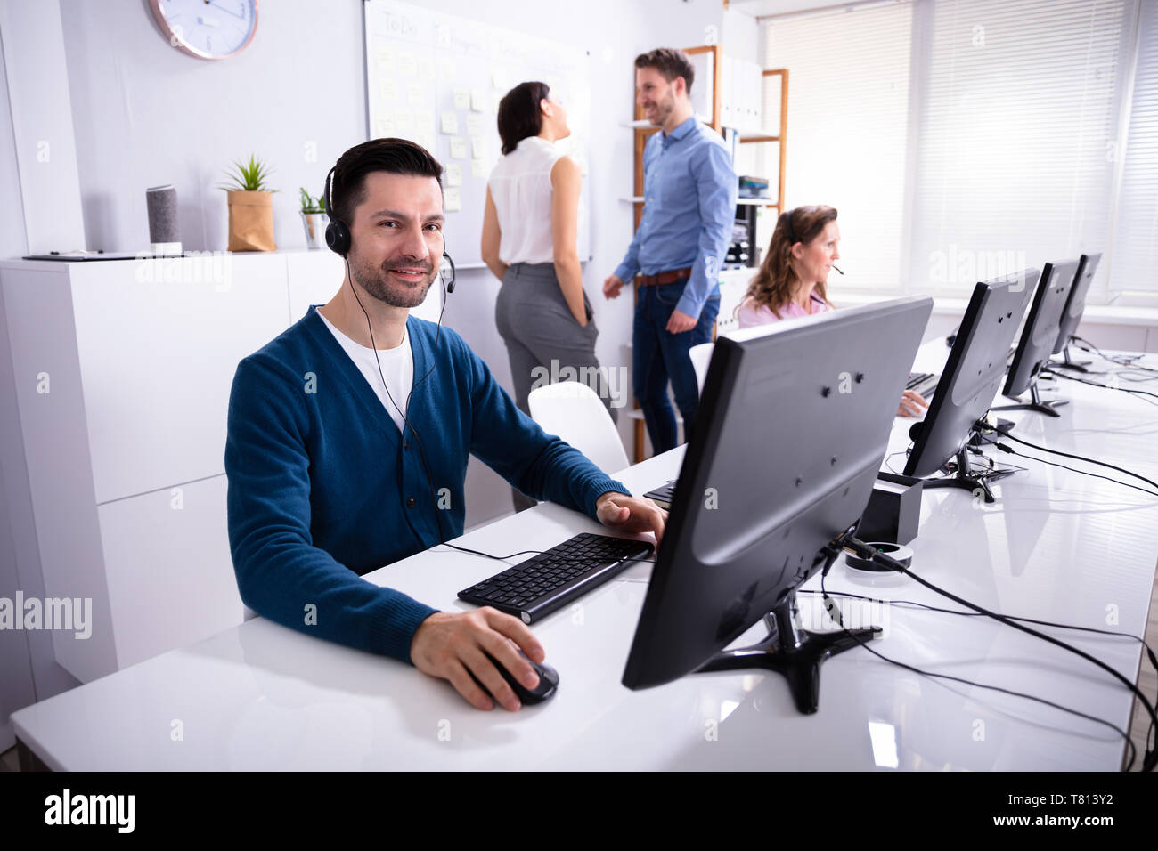 Smiling Young Businessman Working On Computer With Headset In Office Stock Photo