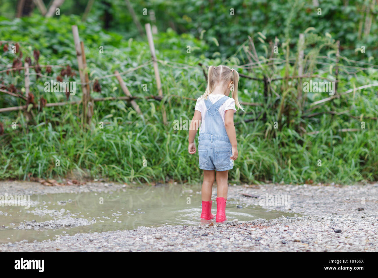 Child in a pink rubber boots in the rain jumping in puddles. Kid playing in summer park Stock