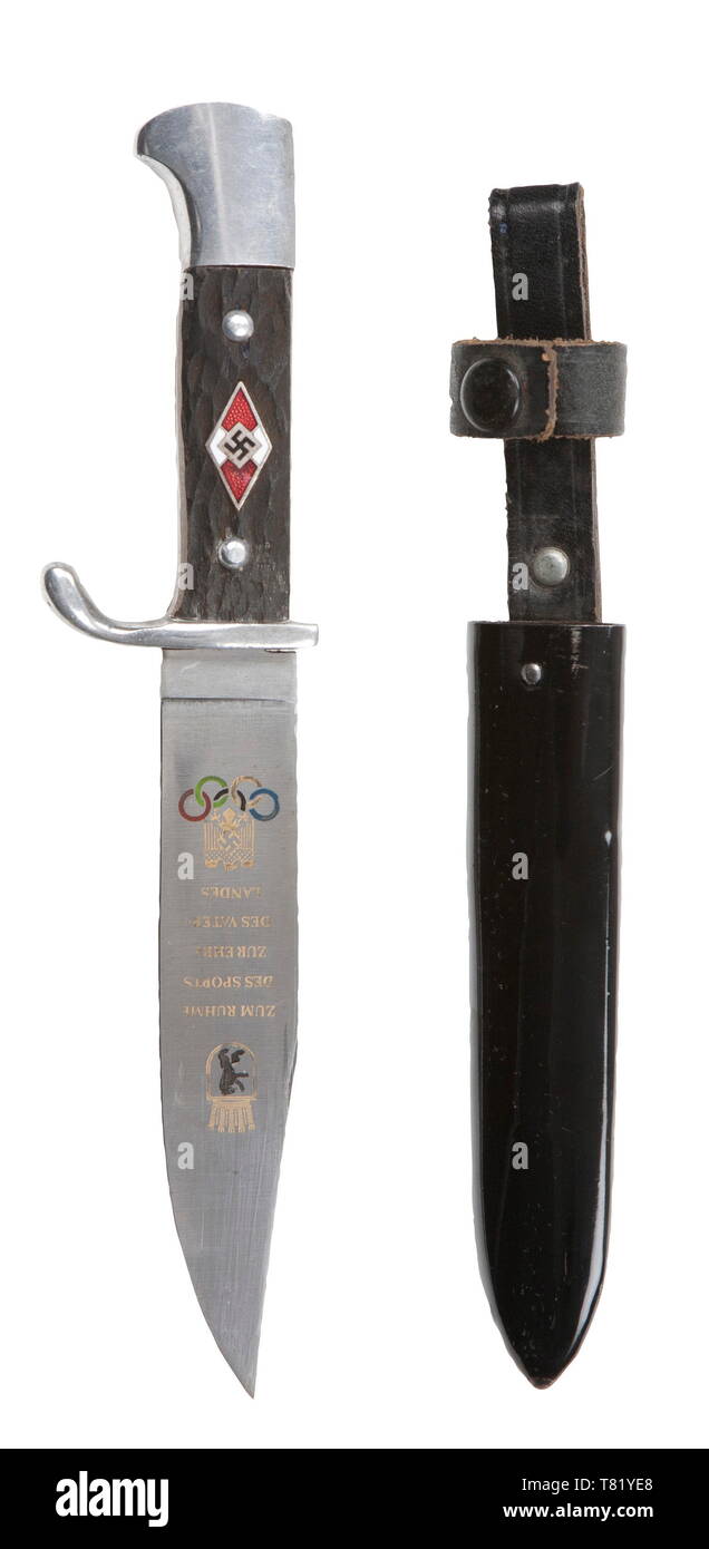 A Hitler Youth knife with etching commemorating the 1936 Olympics. Maker Emil Voss, Solingen. The etched blade with Berlin bear, Olympic Rings, national eagle, and 'Zum Ruhme Des Sports Zur Ehre Des Vaterlandes' (For the glory of sport for the honour of the Fatherland) in colour and gilding. Reverse etched with manufacturer's trademark. Polished aluminium hilt with wooden grip plates simulating stag with enamelled HJ emblem. Black lacquered steel scabbard with black riveted hanger. Complete with brown paper factory issue bag. Length 21 cm. USA-lot historic, historical, 20th, Editorial-Use-Only Stock Photo