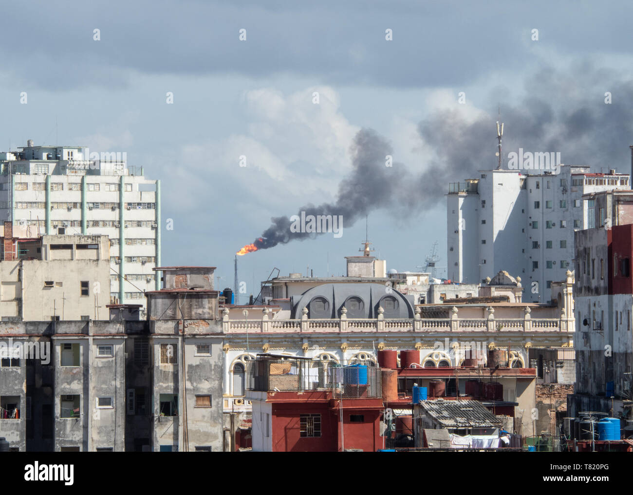 View over rooftops in Old Havana, with oil refinery flame, tower and smoke pollution Stock Photo