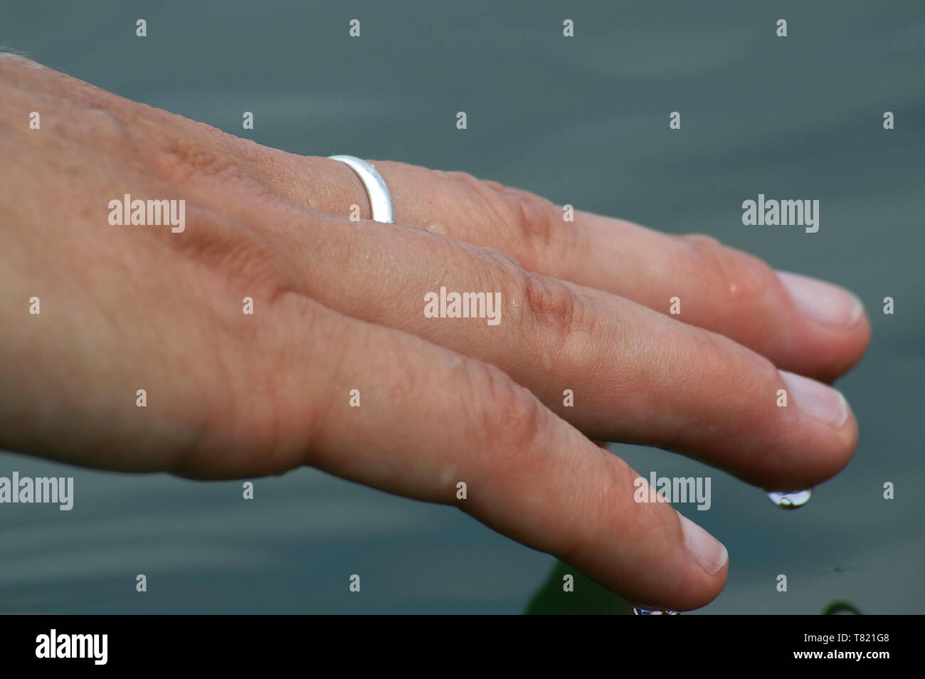 Close-up of a woman's hand touching the smooth surface of a lake. Nahaufnahme der Hand einer Frau, welche die glatte Oberfläche von einem See berührt. Stock Photo