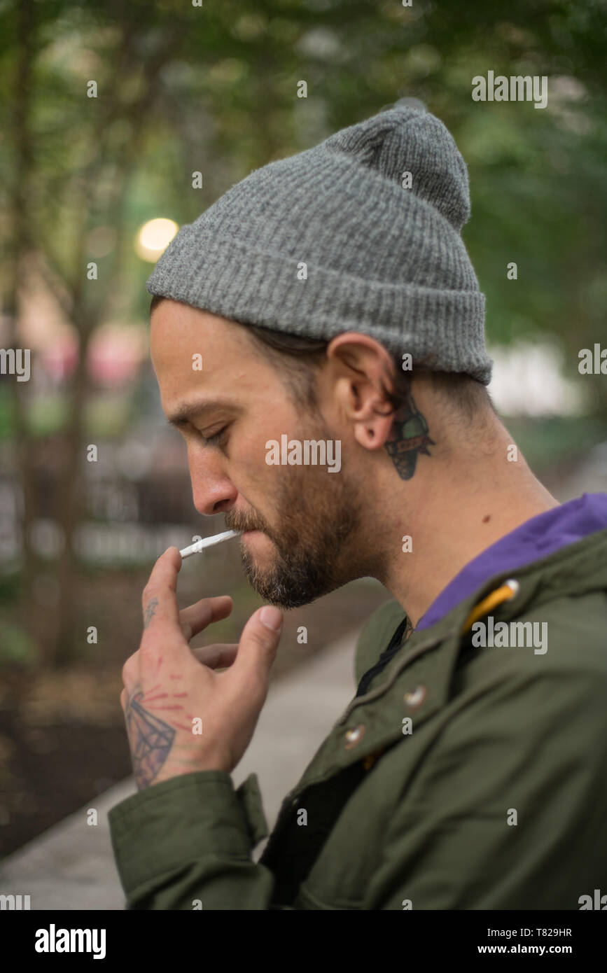 street portrait taken in Philadelphia Pennsylvania of a young caucasian man in a hoodie smoking a cigarette outside Stock Photo