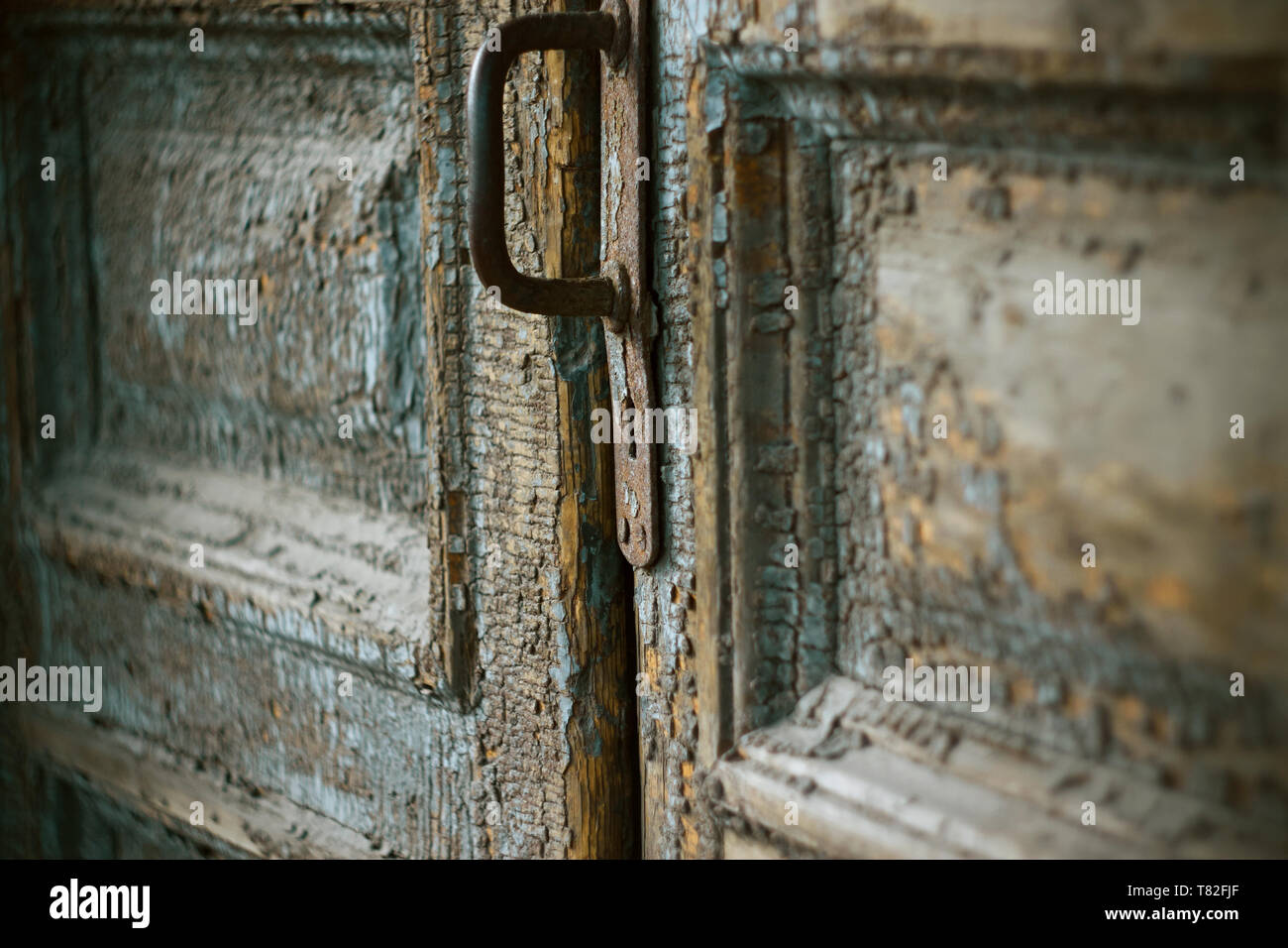 An old medieval closed door with a crumbling layer of blue paint, with a rusty iron handle and a keyhole, which you want to peek. Stock Photo