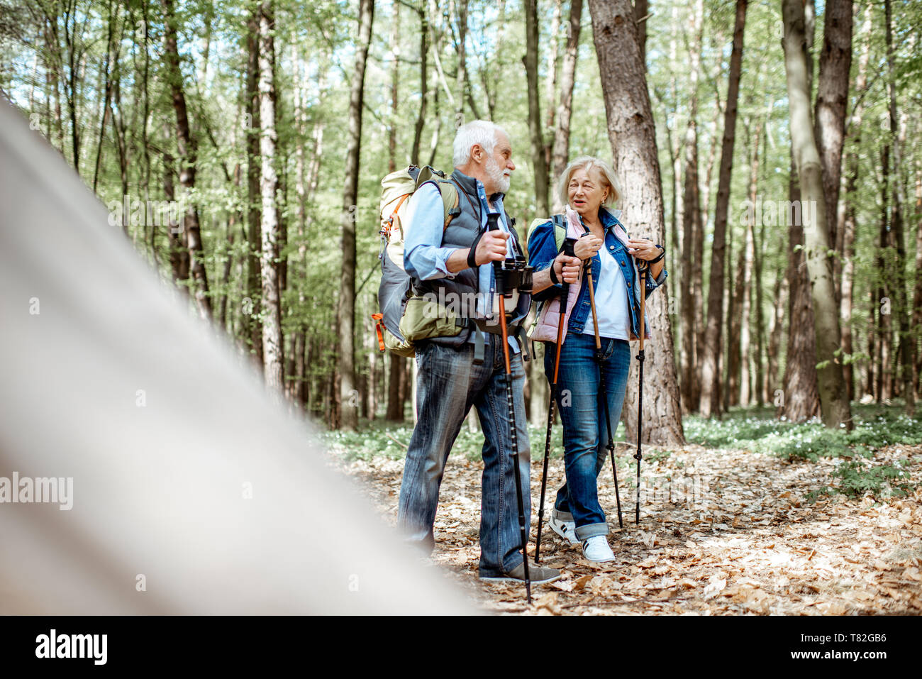 Beautiful senior couple hiking with backpacks and trekking sticks in the forest. Concept of active lifestyle on retirement Stock Photo