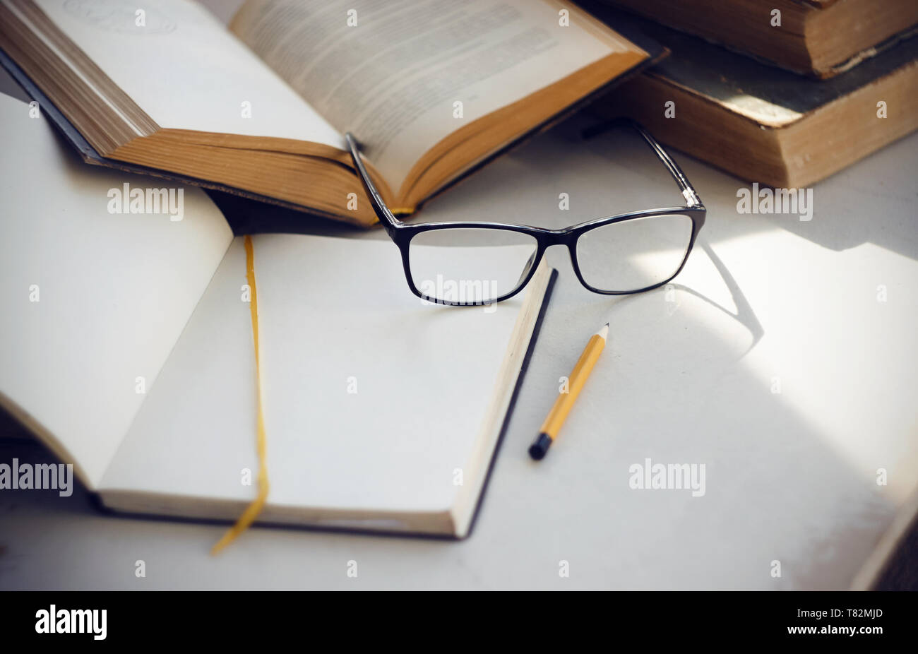 Items needed for scientific research: ancient encyclopedias, a notebook with a yellow bookmark , glasses, a yellow pencil and an open book with inform Stock Photo