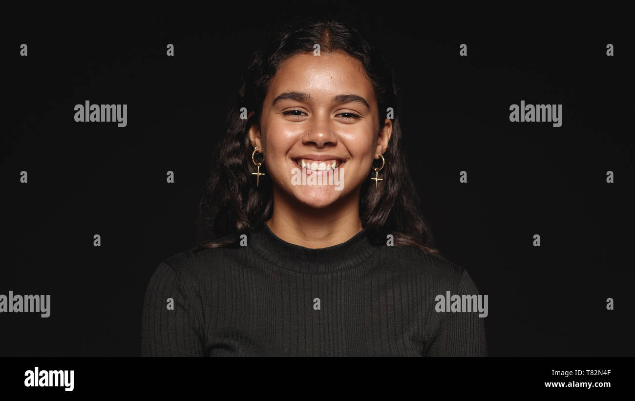 Close up of a smiling woman against black background. Young woman with a cute smile looking at camera. Stock Photo