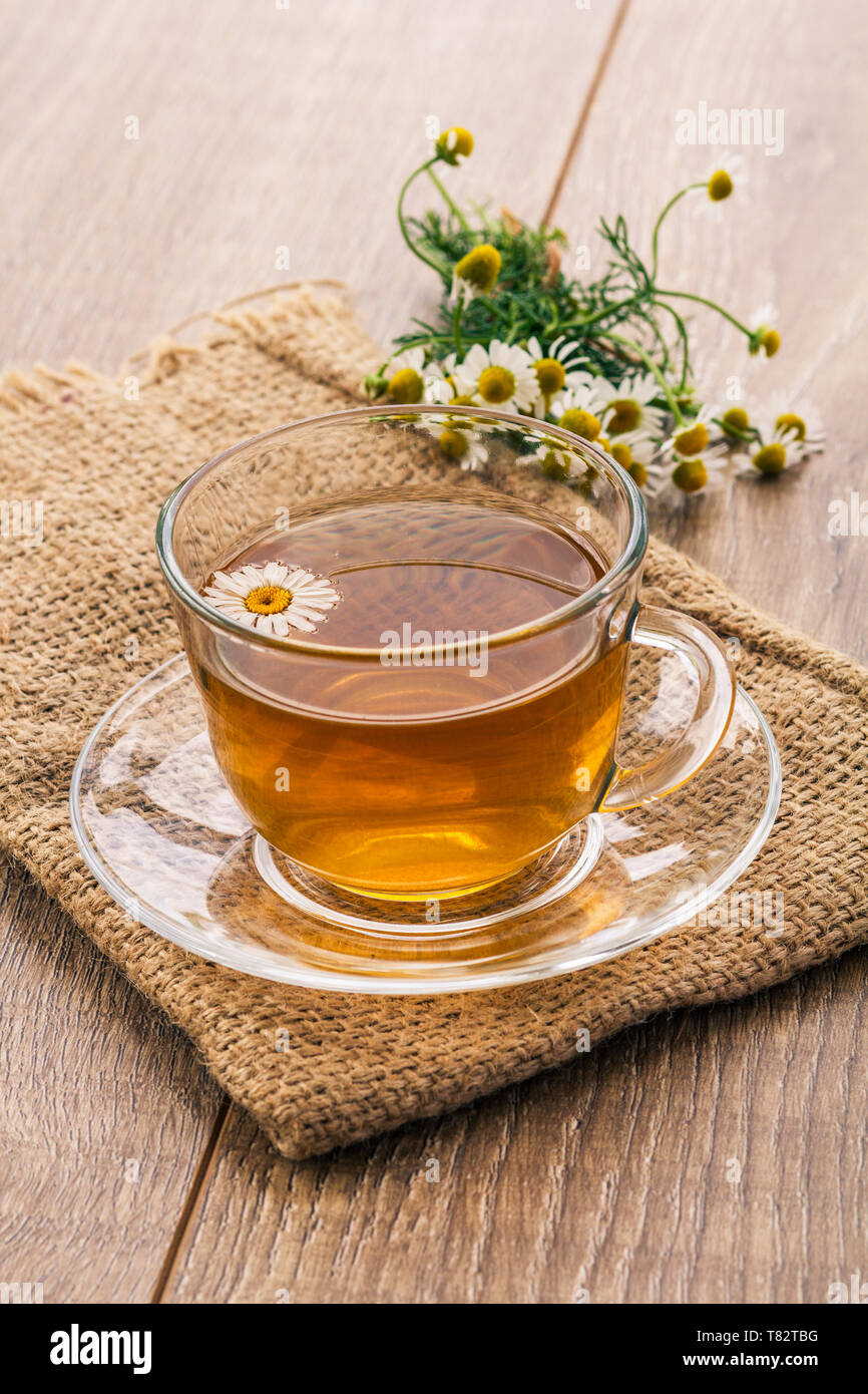 Glass cup of green tea with white chamomile flowers and sack on wooden ...