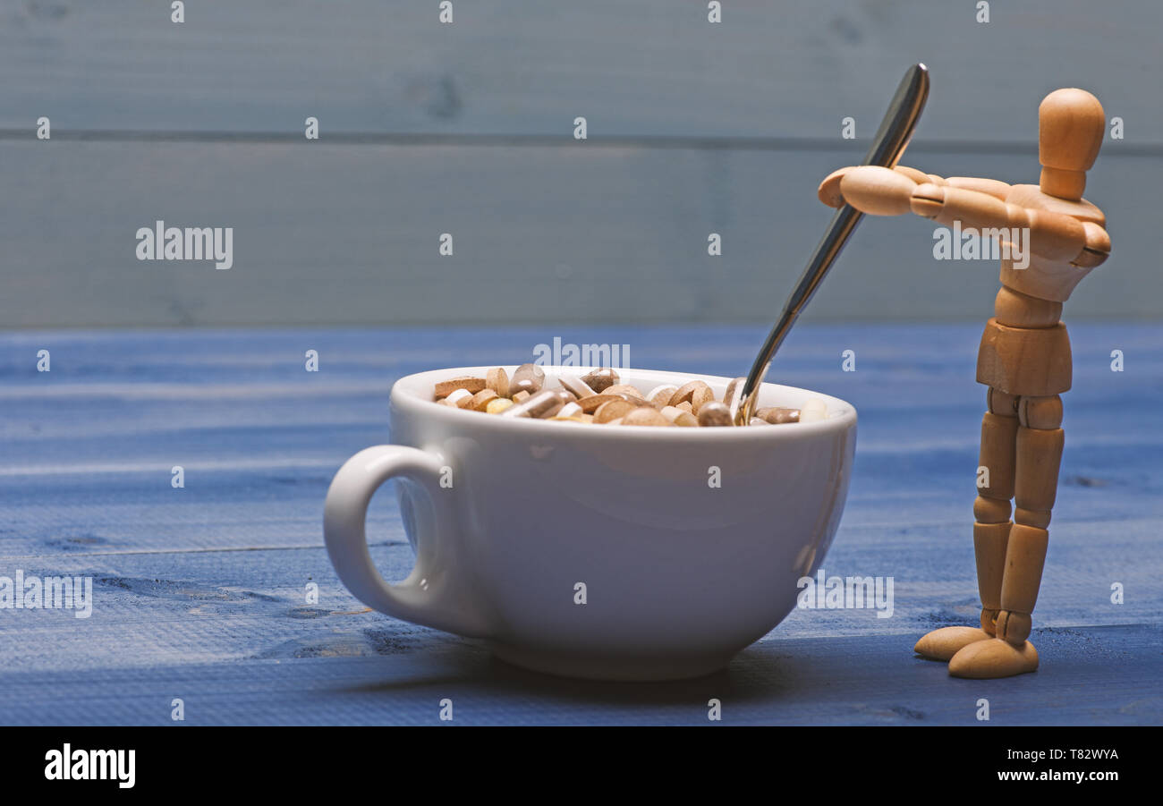 Medicines dose. Wooden human dummy near cup full pills and tablets