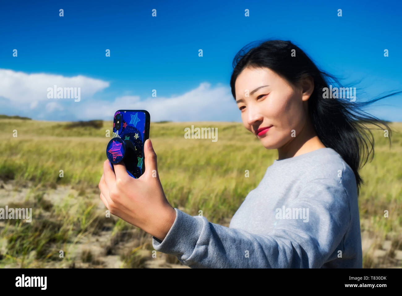 A chinese woman taking a selfie on a sunny windy day on the cape cod national seashore in Truro Massachusetts. Stock Photo