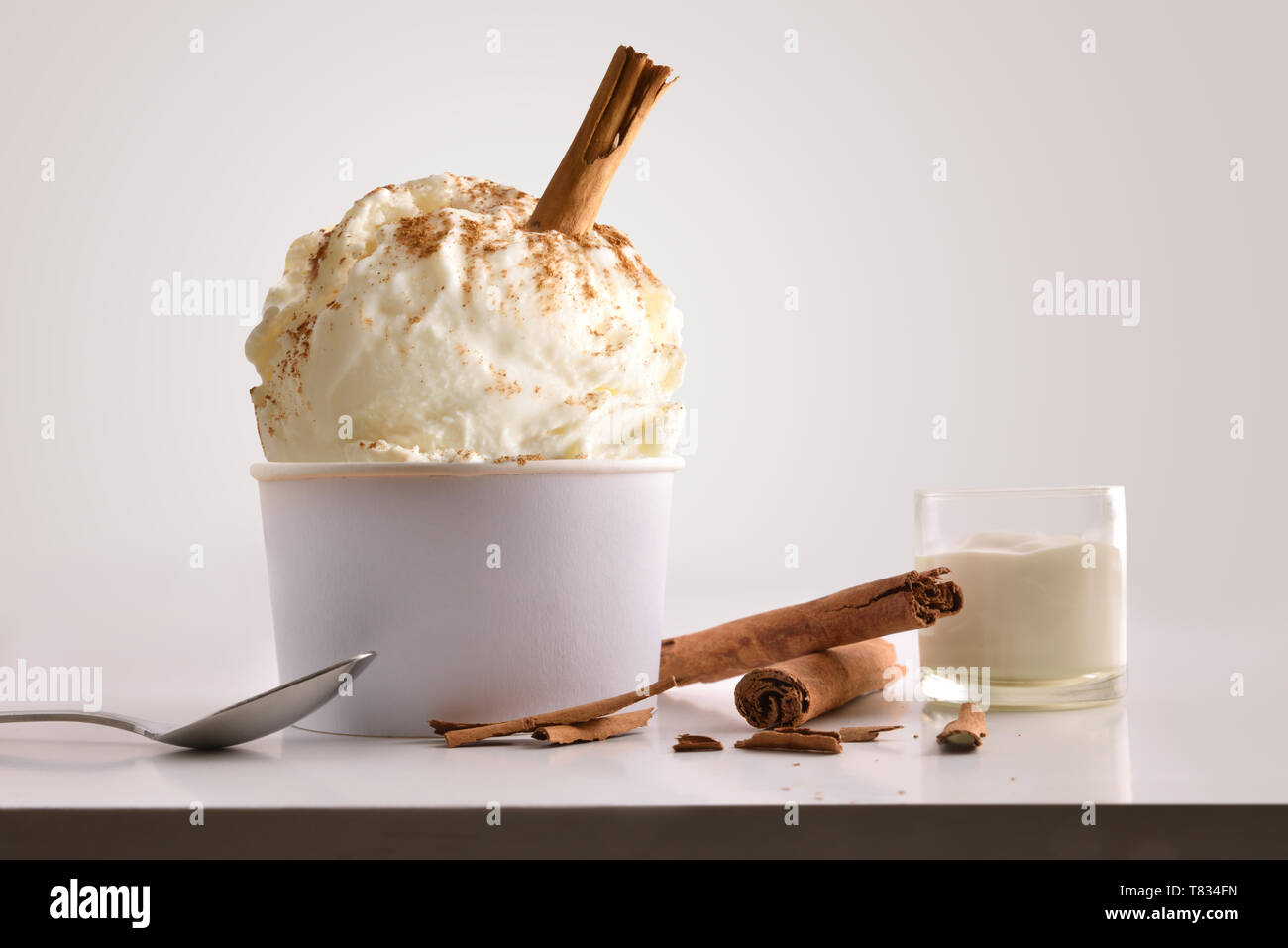 Composition of cinnamon ice cream ball in paper cup on white table with products of ornament and elaboration isolated background. Horizontal compositi Stock Photo