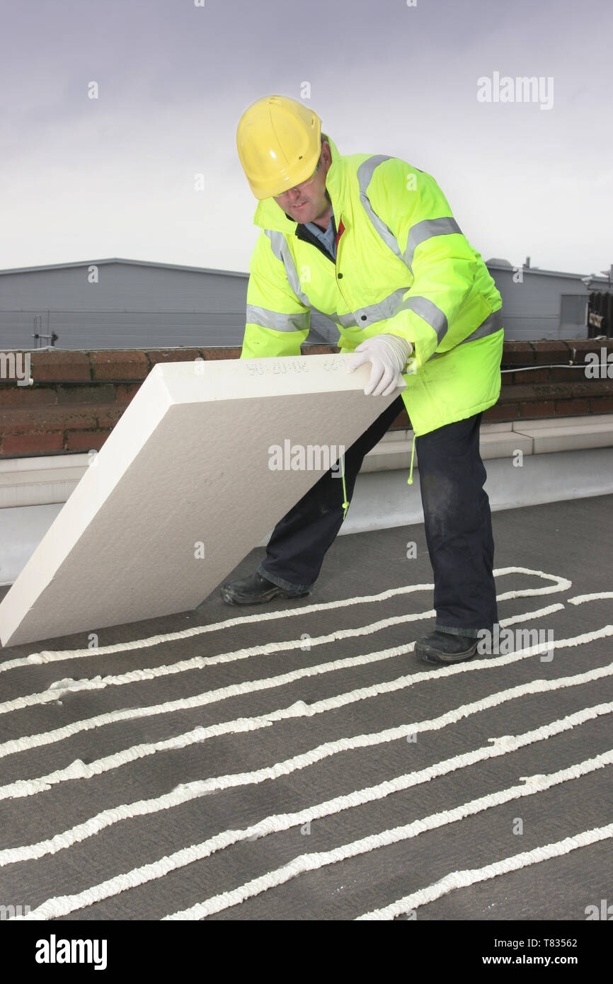 A builder installs additional thermal insulation onto a flat roof by placing  insulation blocks onto sprayed adhesive foam. Stock Photo