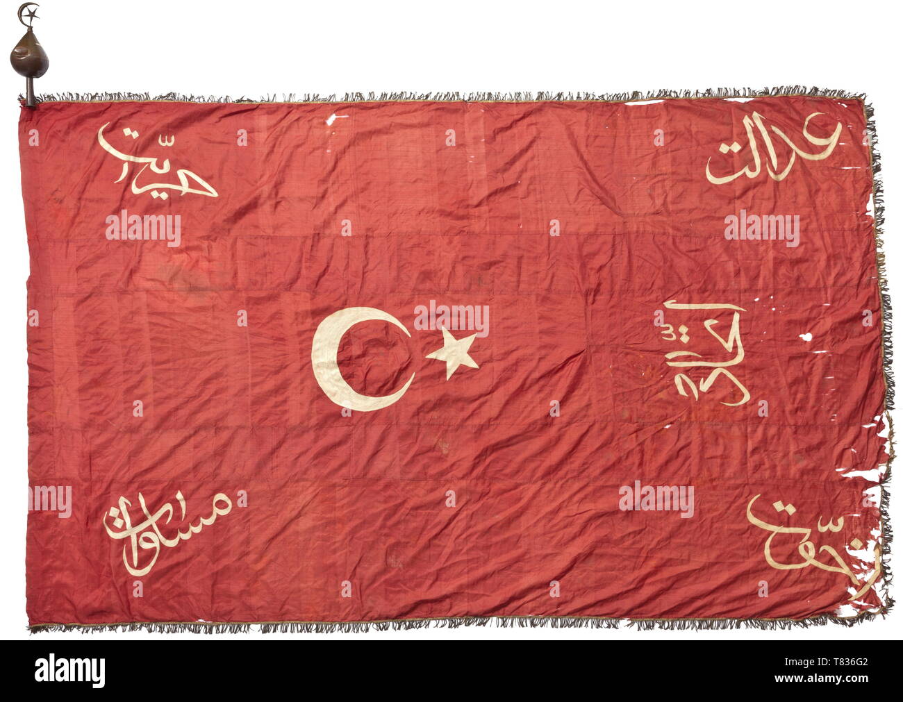 A flag of the Young Turks Movement Circa 1908. Fine dark red silk, five-piece cloth with gold fringe edging on three sides (darkened), guide for the flag pole and crescent moon and the following inscriptions in white chain stitch embroidery: 'Adalet' (justice), 'Hürriyet' (liberty), 'Müsavit' (equality), 'Uhuvvet' (fraternity) and 'Ittihat' (unity). Signs of age and small flaws. Size circa 250 x 160 cm. Also a corresponding flag finial of sheet brass (dents) with traces of gilding. The Young Turks Movement was founded in the late 19th century in , Additional-Rights-Clearance-Info-Not-Available Stock Photo