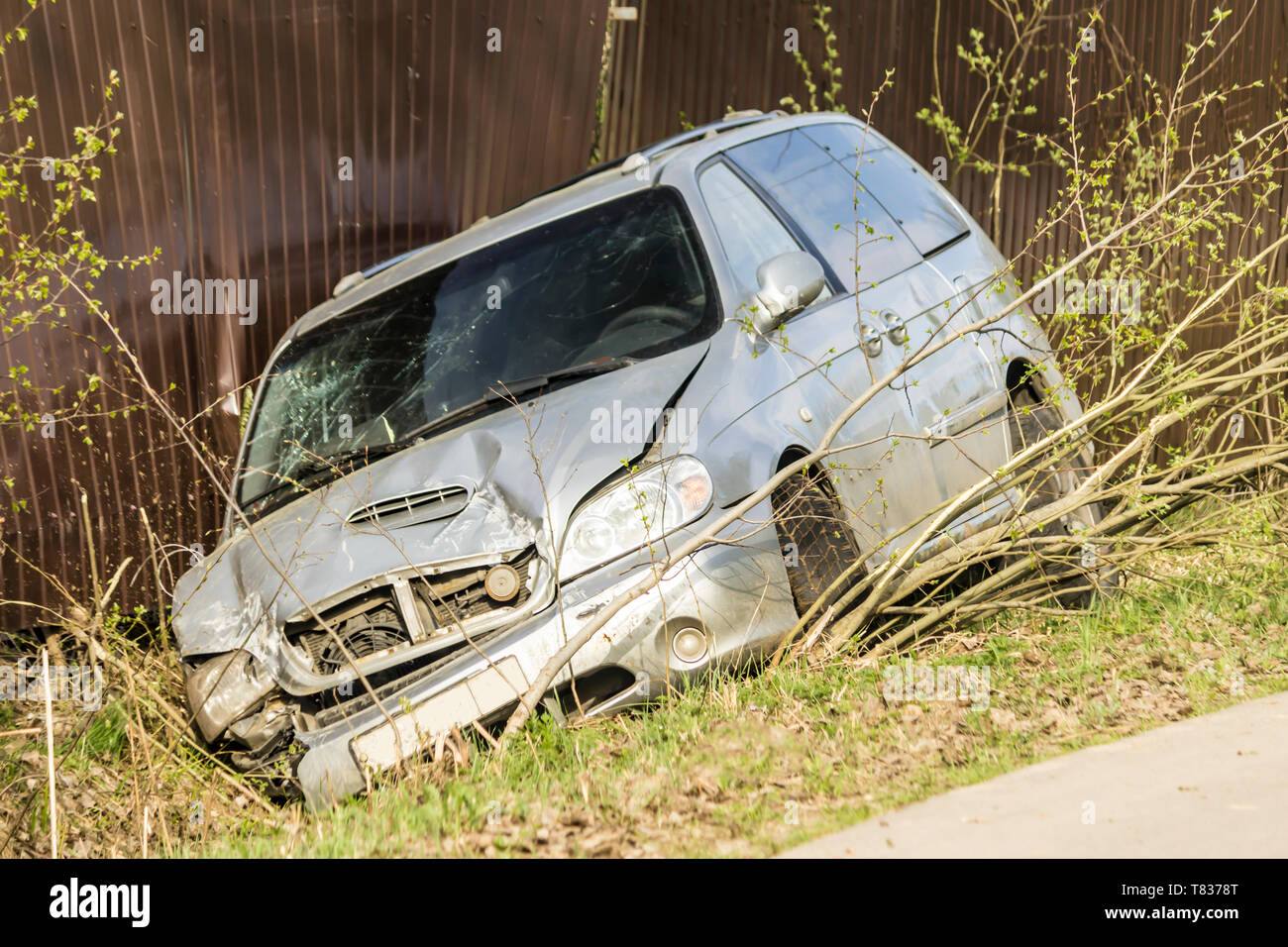 Car accident on a country road. The car is broken in front, slid into a ditch and damaged a metal fence. Stock Photo