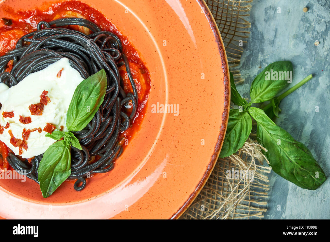 Spaghetti with cuttlefish ink with cream sauce on an orange plate. Gray textured background with beige fabric. Beautiful serving of dishes. Restaurant menu Stock Photo