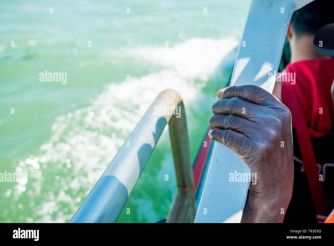 close up of thin and skinny african migrant man hand on boat while crossing mediterranean sea to europe on sunny day Stock Photo