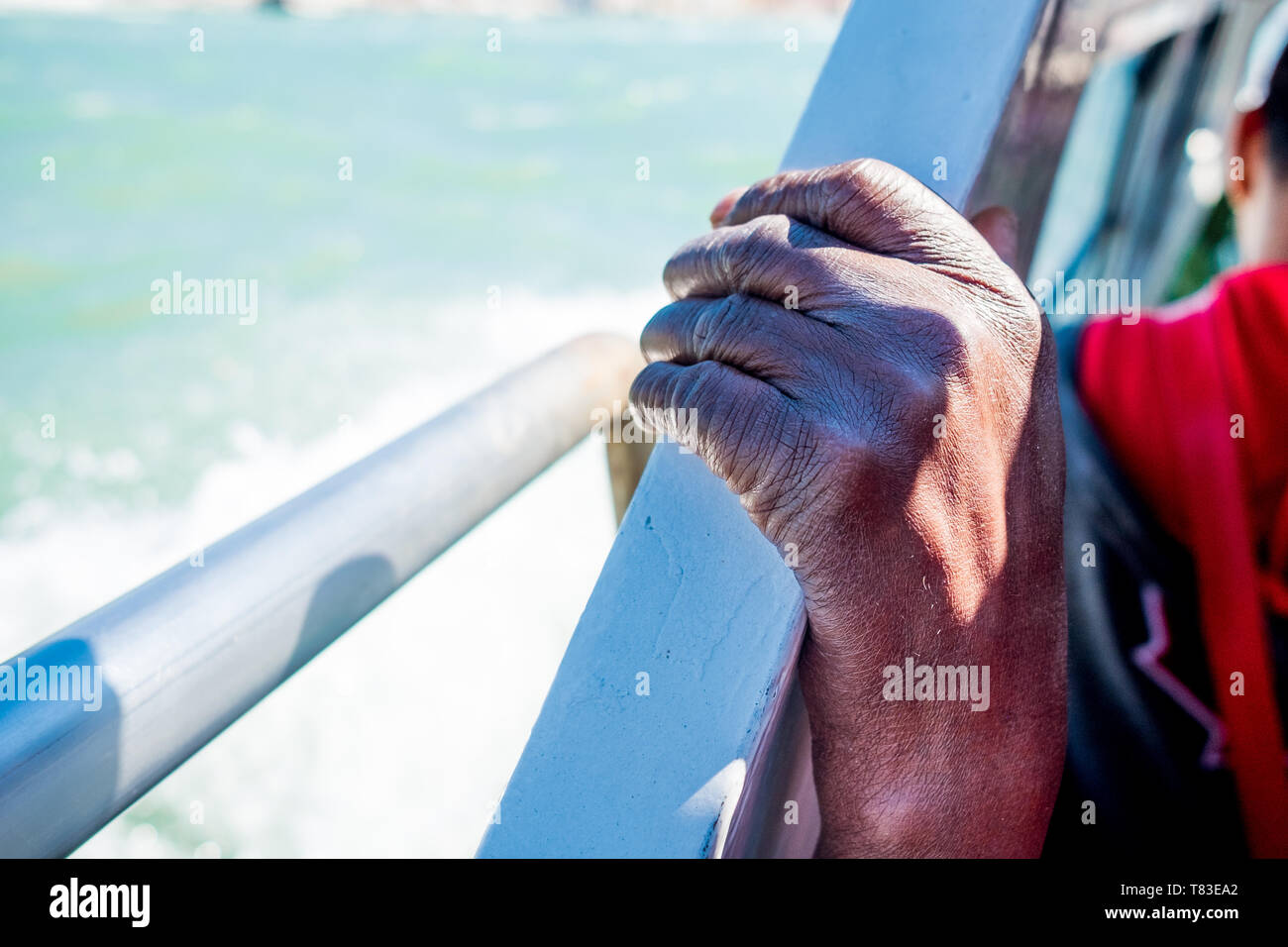 close up of thin and skinny african migrant man hand on boat while crossing mediterranean sea to europe on sunny day as symbol of refugees crisis Stock Photo