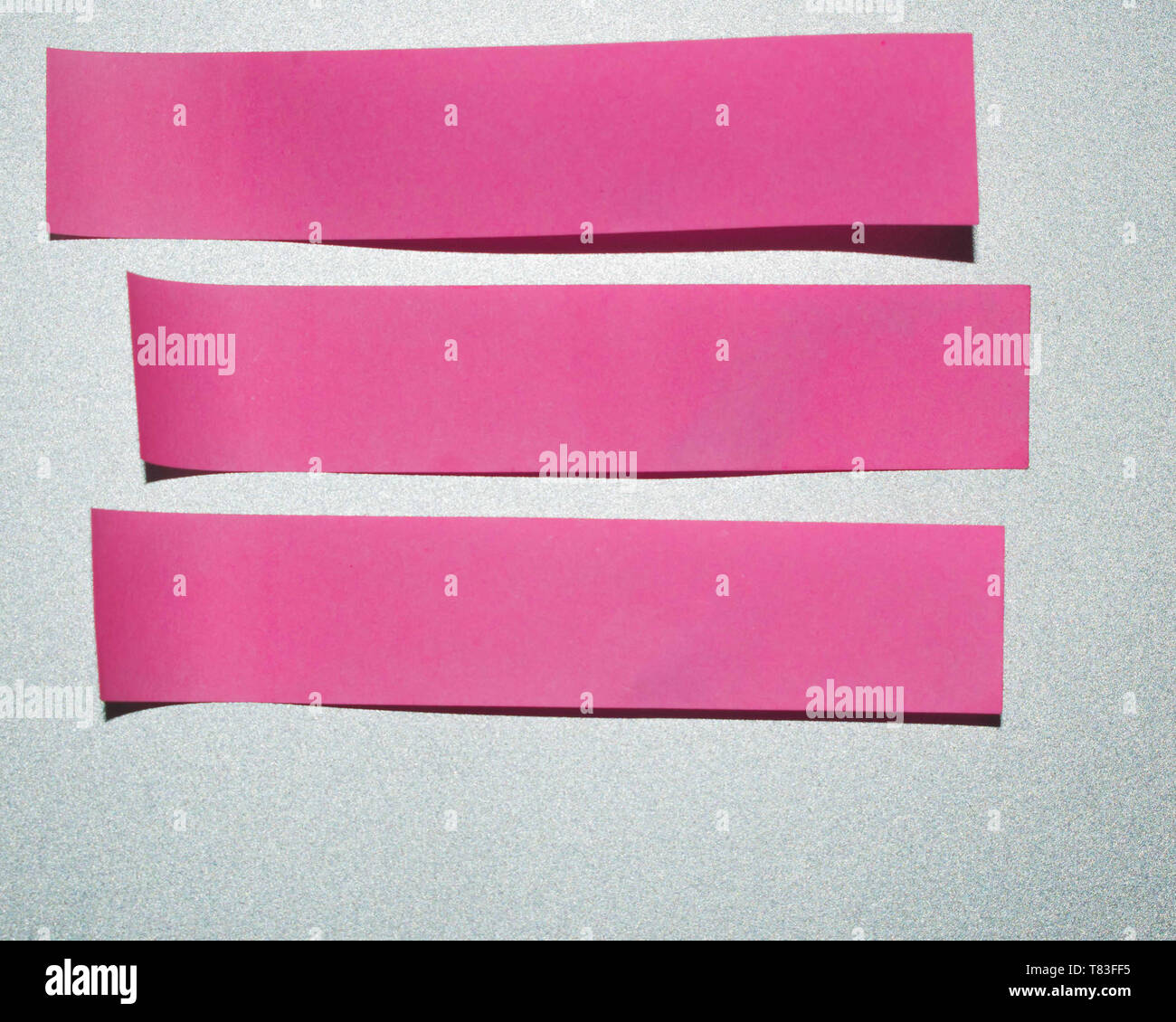 Pink small elongated sticky notes. Three blank pink sticky notes on a silver background. Stock Photo