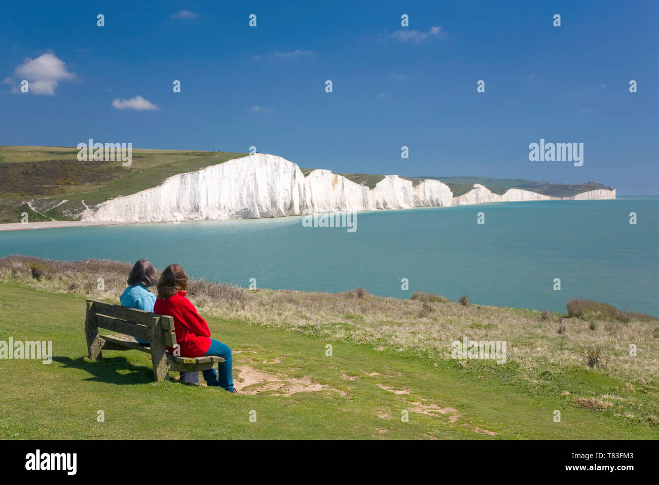 Cuckmere Haven, East Sussex, England. Visitors on bench admiring view across the bay from Seaford Head to the Seven Sisters cliffs. Stock Photo