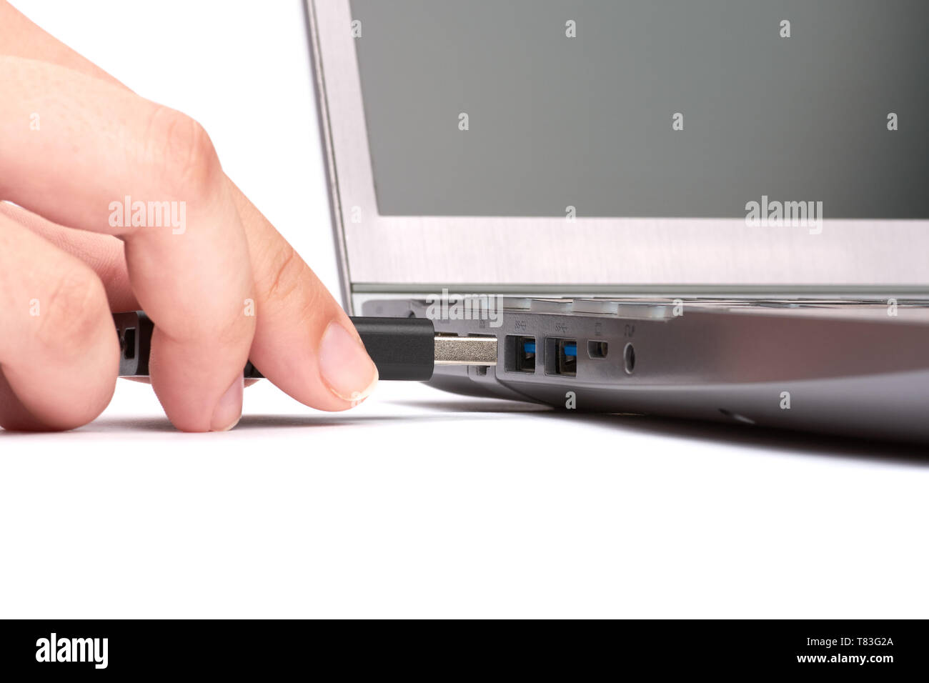 The hand of a young woman connects a USB flash drive to a port in a silver laptop with a black keyboard. Isolated on white background. Stock Photo