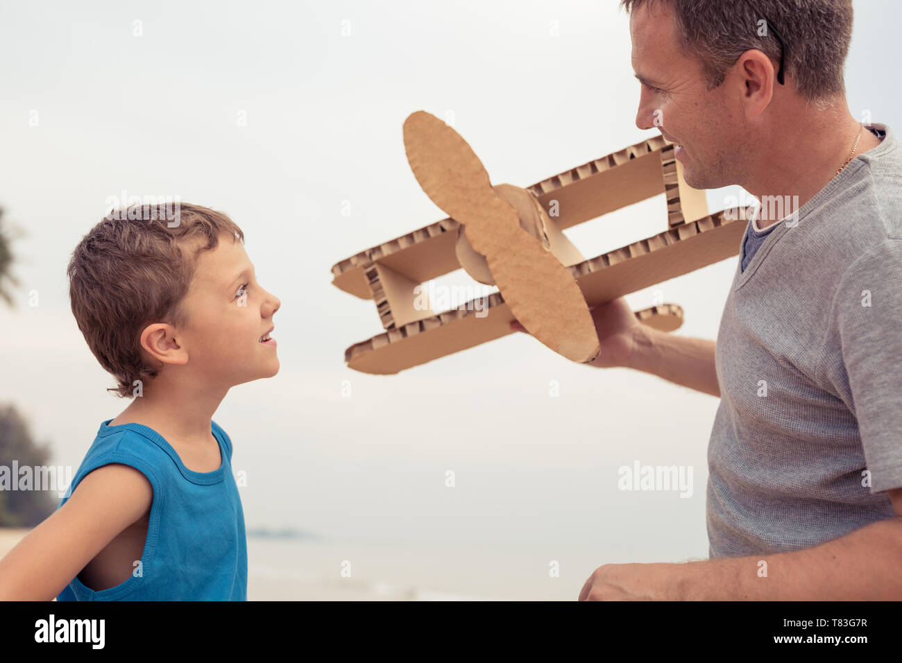Father and son playing with cardboard toy airplane in the park at the day time. Concept of friendly family. People having fun outdoors on the beach. Stock Photo