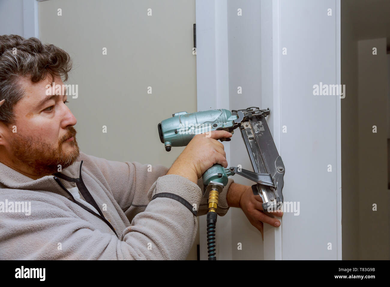 Carpenter using nail gun to moldings on door, framing trim, with the