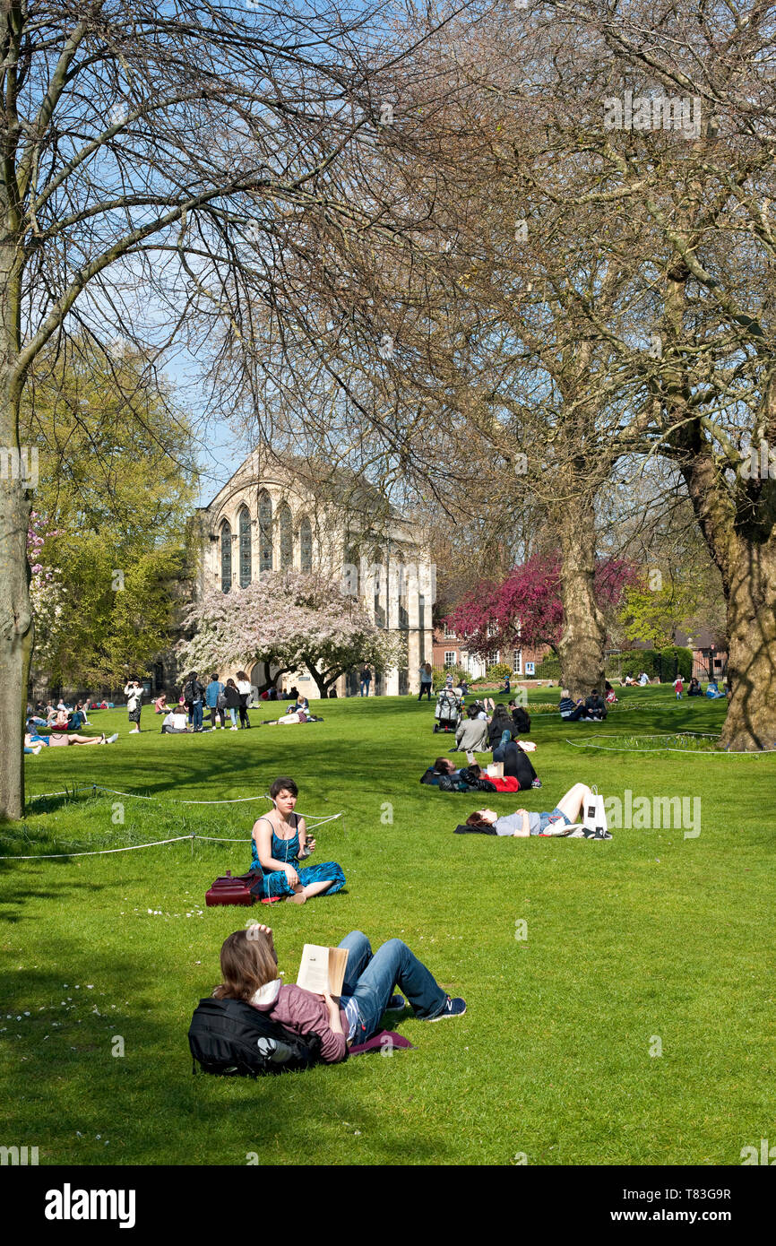 People tourists visitors sitting reading and relaxing in the spring sunshine Deans Park York North Yorkshire England UK United Kingdom Great Britain Stock Photo