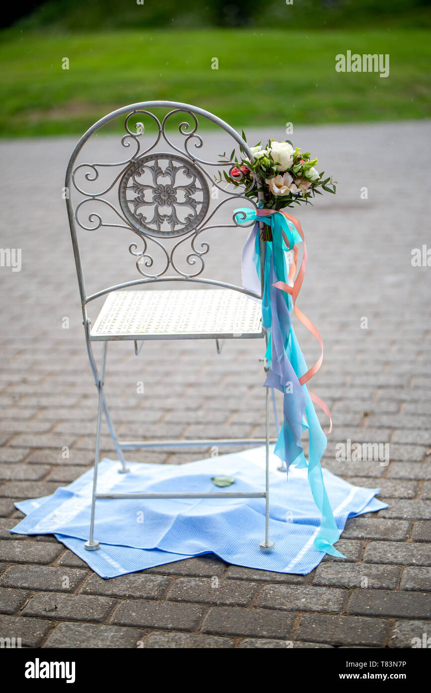 Chair decorated with bouquet of flowers and ribbons in wedding ceremony Wedding chair is placed on towels. Stock Photo