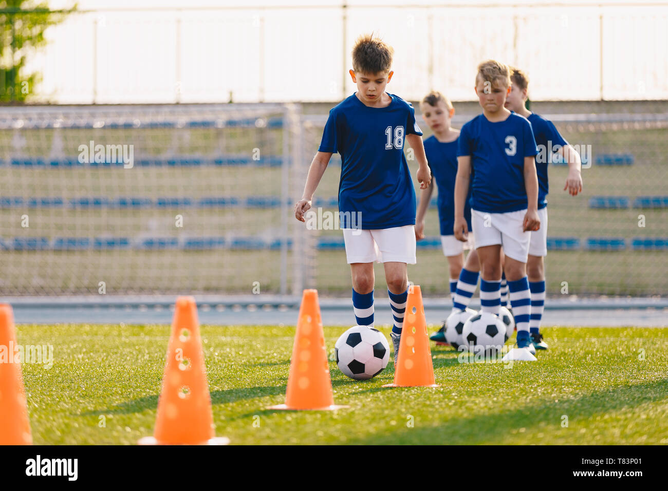 Soccer camp for kids. Boys practice football dribbling in a field. Players develop soccer dribbling skills. Children training with balls and cones Stock Photo