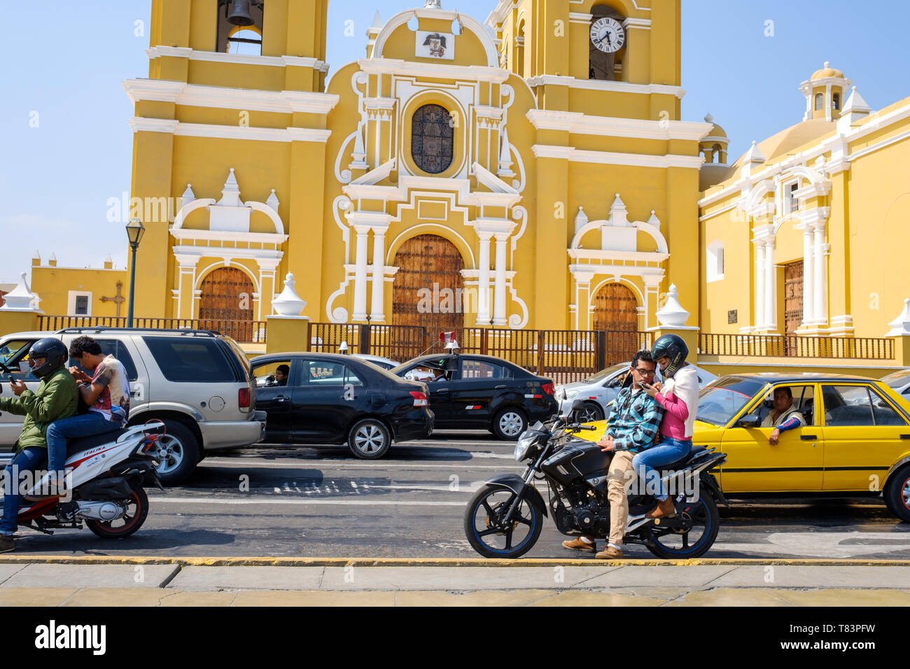 Motorbike driver checking the mobile phone in front of the Cathedral of Trujillo at the Plaza de Armas or Main Square of Trujillo, Peru Stock Photo