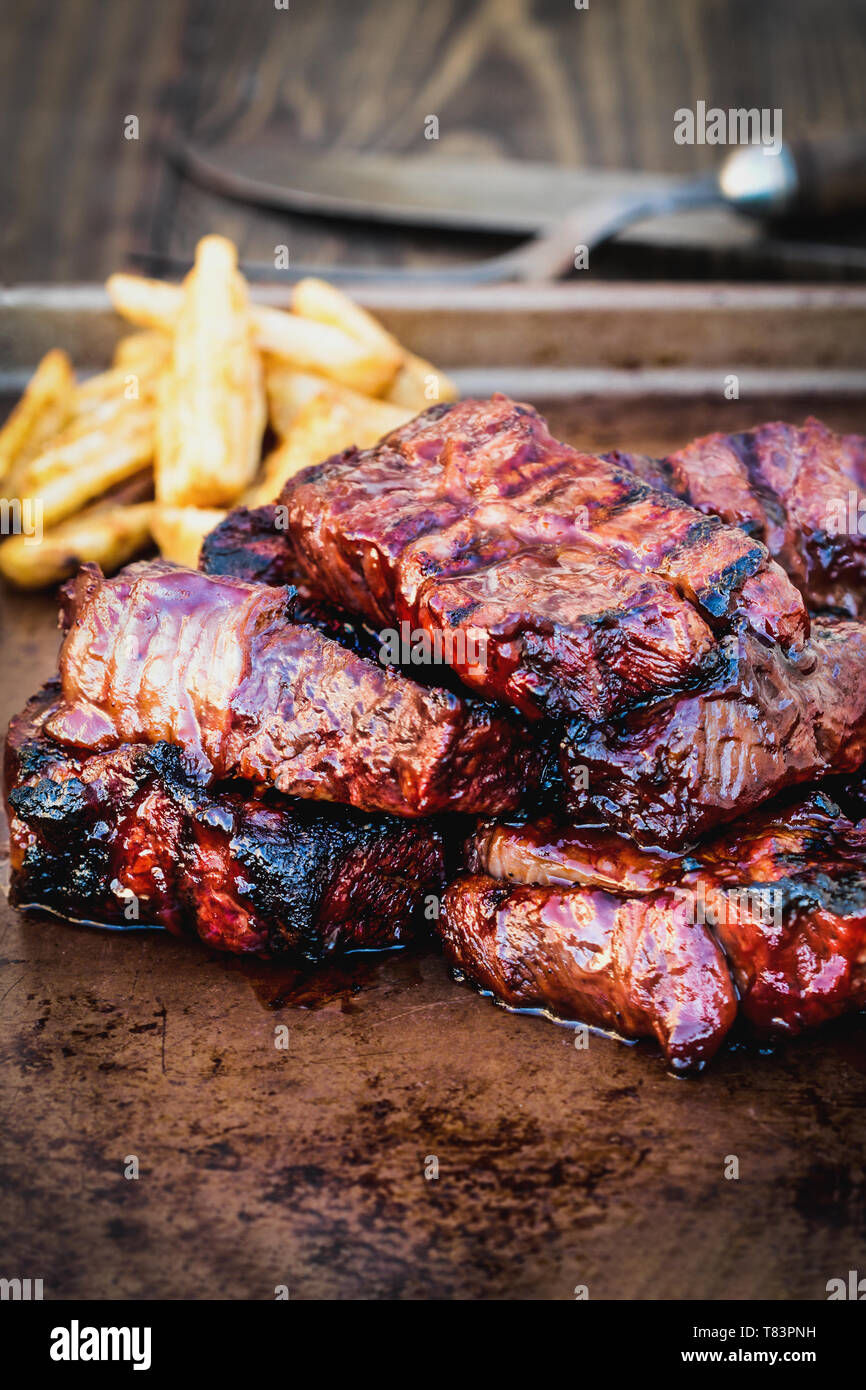 Bbq boneless beef ribs with barbecue sauce and potato wedges over a rustic background. Extreme shallow depth of field with blurred background and sele Stock Photo