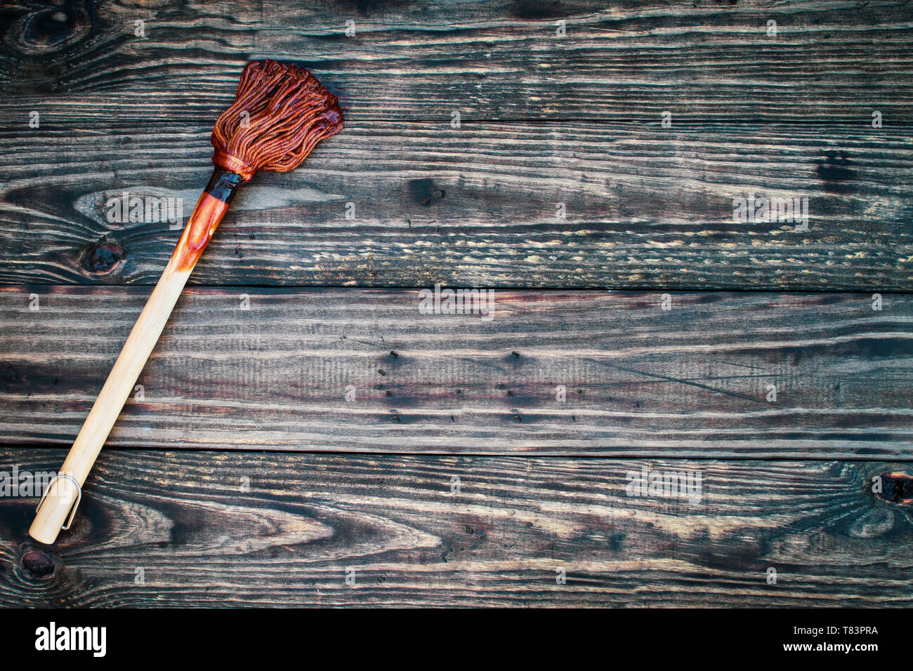BBQ Mop or brush over top a rustic wood table / background with barbecue sauce on end. Image shot from overhead view. Stock Photo