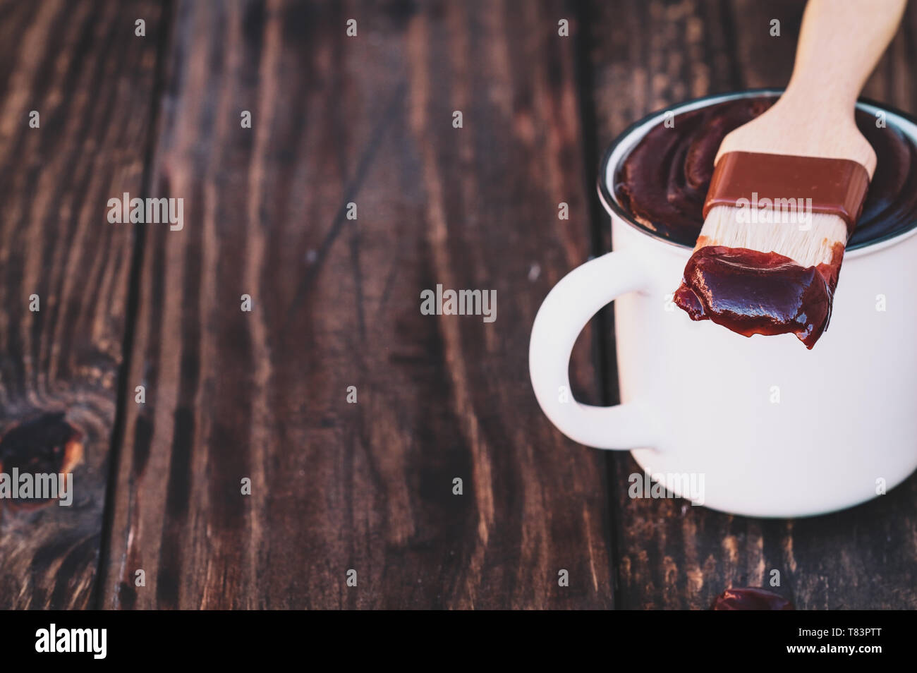 BBQ brush with barbecue sauce on the tip resting on a white cup over a
