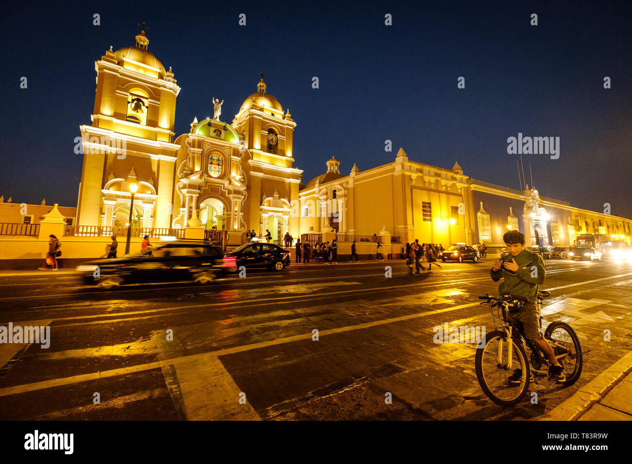 Biker checking the mobile phone at night in front of the Cathedral of Trujillo at the Plaza de Armas or Main Square of Trujillo, Peru Stock Photo