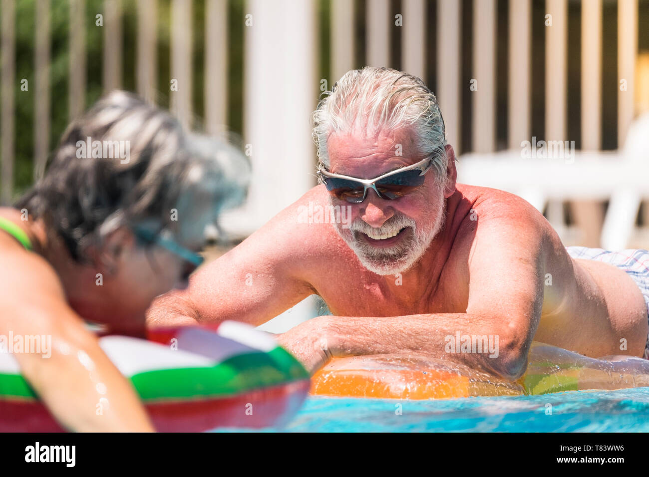 Cheerful happy smiling people senior man enjoying the summer swimming pool in couple retired nice lifestyle - white hair and summer holiday vacation o Stock Photo