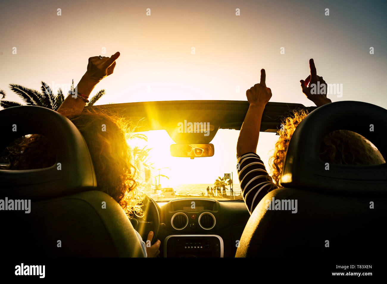 People happy for travel vacation with convertible car giving up hands and dancing for the sea summer holiday vacation - sun on the horizon and joyful  Stock Photo