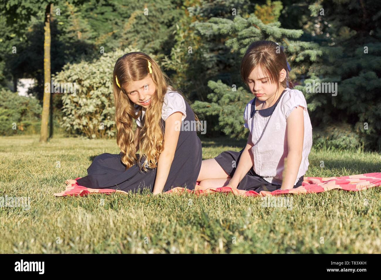 Portrait of two girls friends 7, 8 years old sitting on the grass in the park, golden hour Stock Photo
