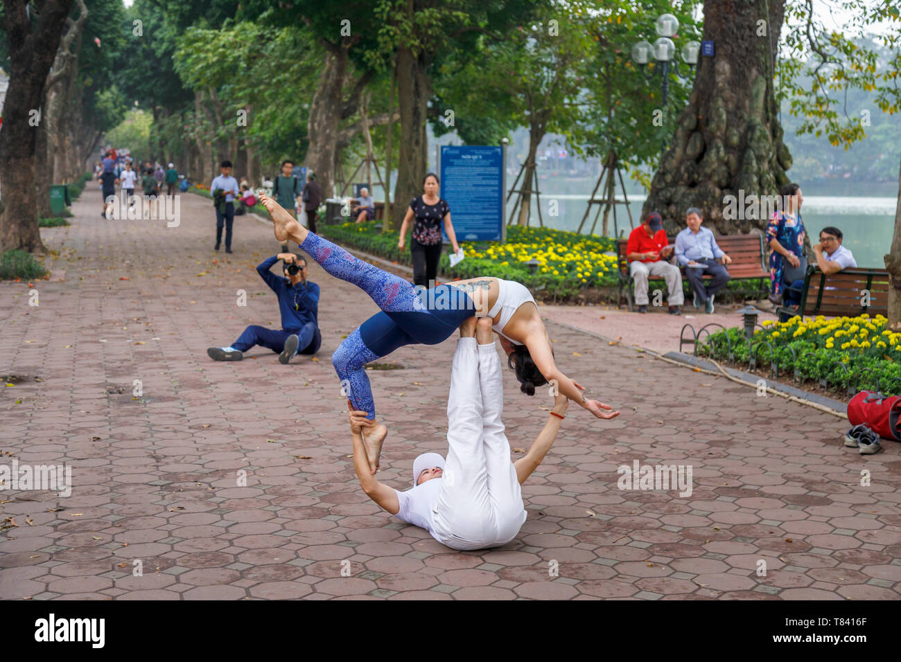 A young couple perform acrobatics on the pavement on the side of Hoan Kiem Lake in the historic centre of Hanoi, north Vietnam, south-east Asia Stock Photo