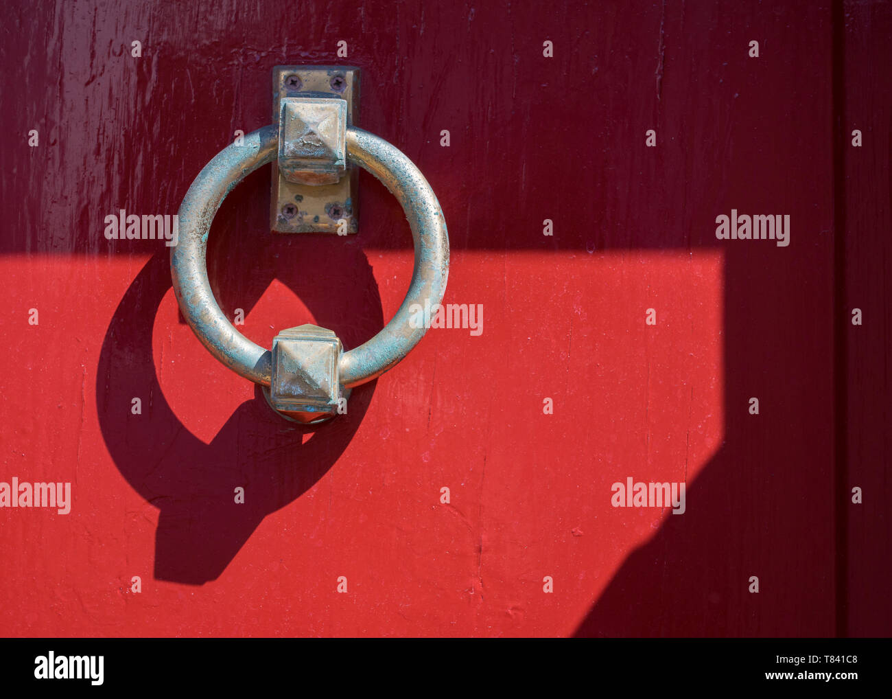 A circular metal door knocker on a bright red wooden door, Stavanger, Norway. Stock Photo