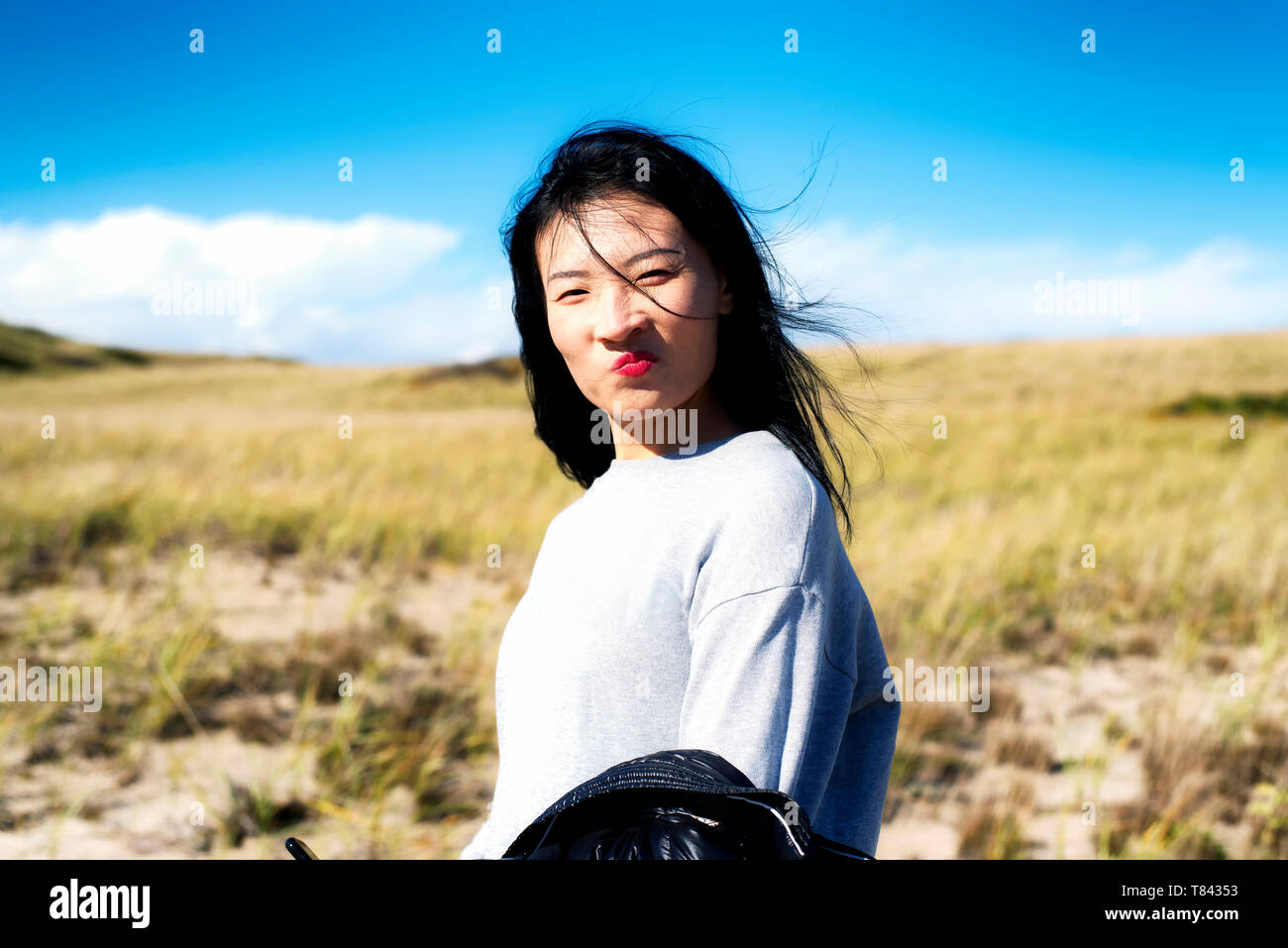 A chinese woman making a funny face outside on a sunny windy day on the cape cod national seashore in Truro Massachusetts. Stock Photo