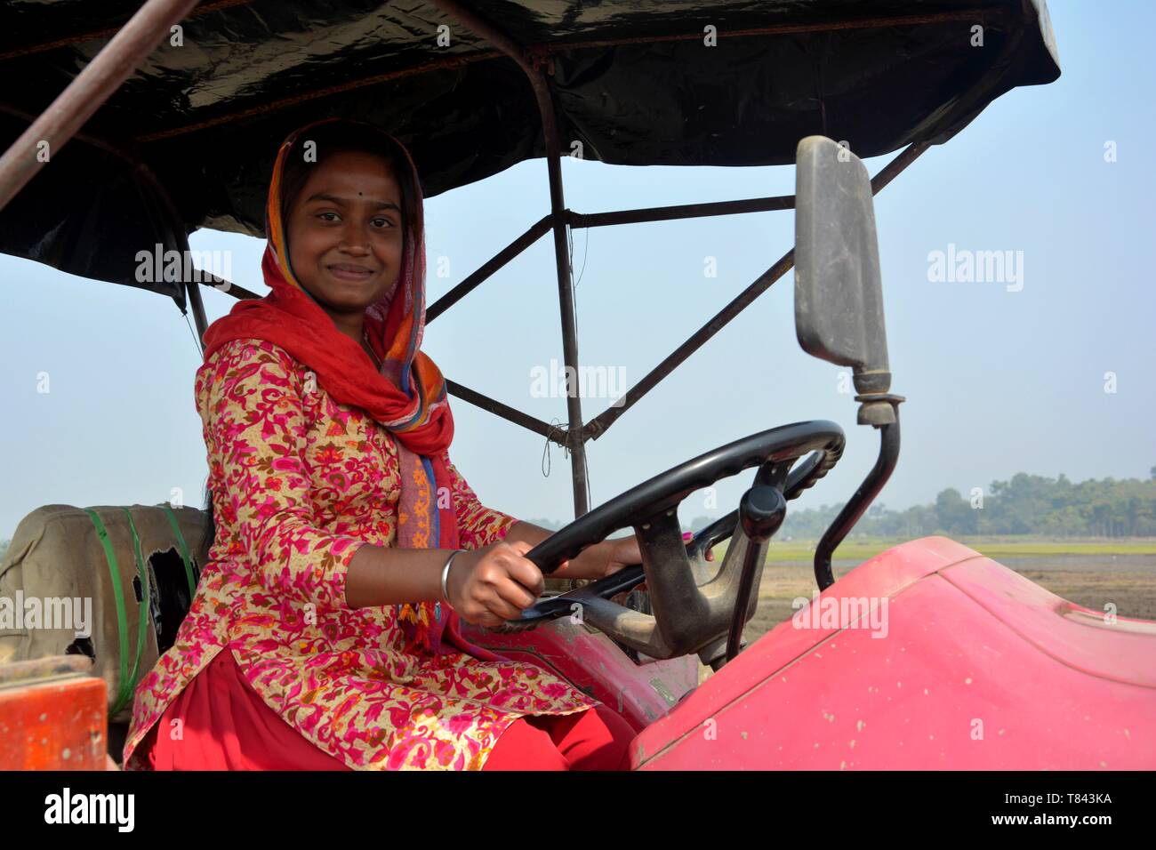 Close up of  an Indian girl sitting on a tractor in the field with sky in the background, selective focusing. Stock Photo