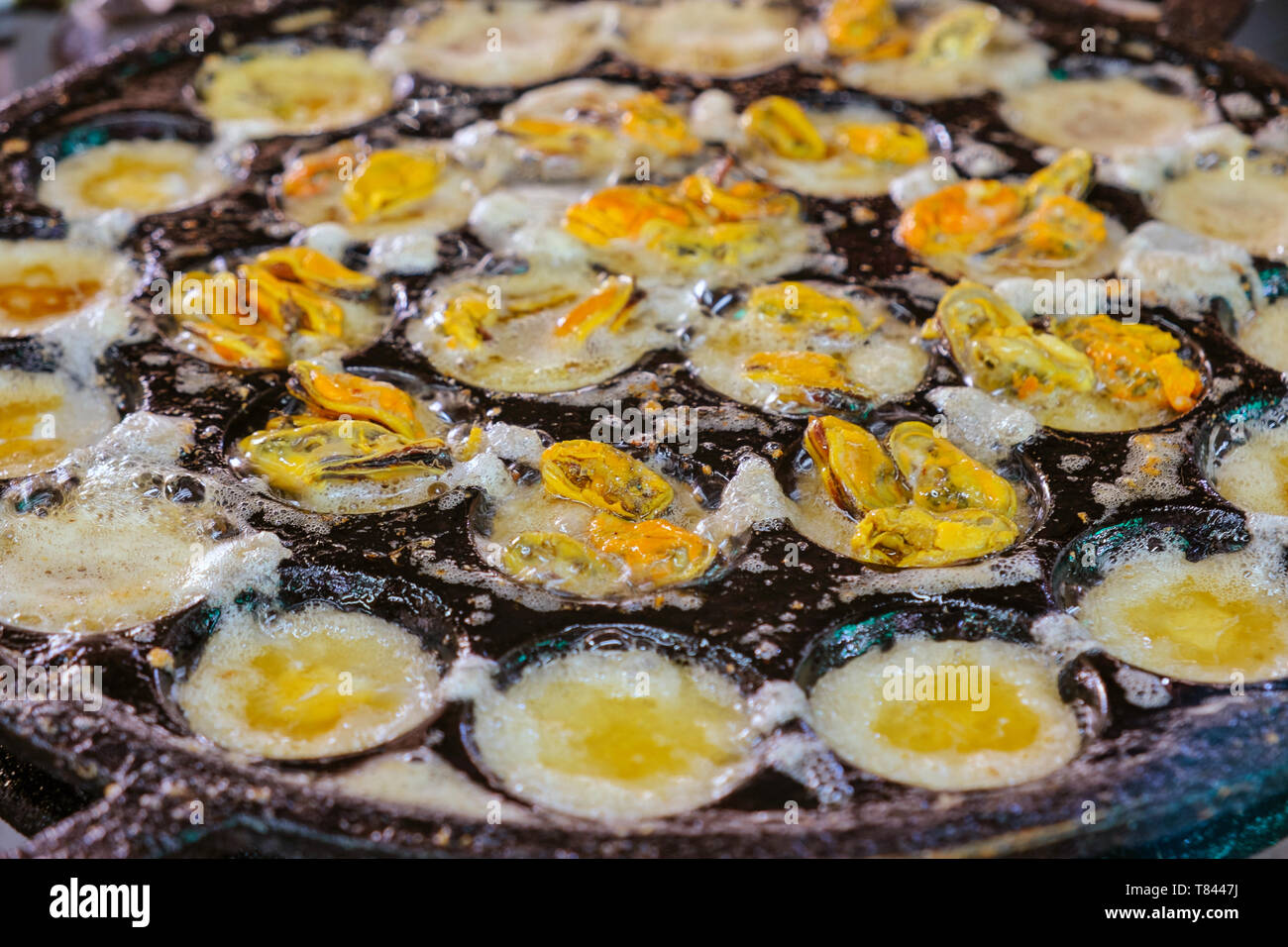 Fried egg with mussels boiling in Kanom Krok iron pan. Thai seafood for sale in the market, Bang Krachao. Street food in Thailand. Stock Photo