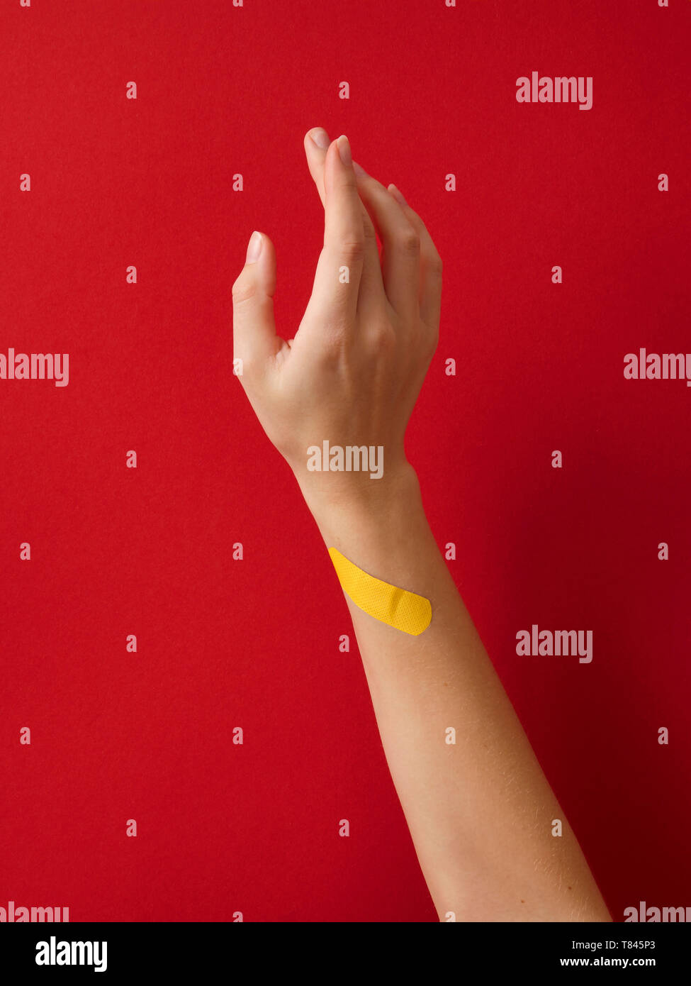 First aid adhesive plaster on woman's wrist against red background Stock Photo