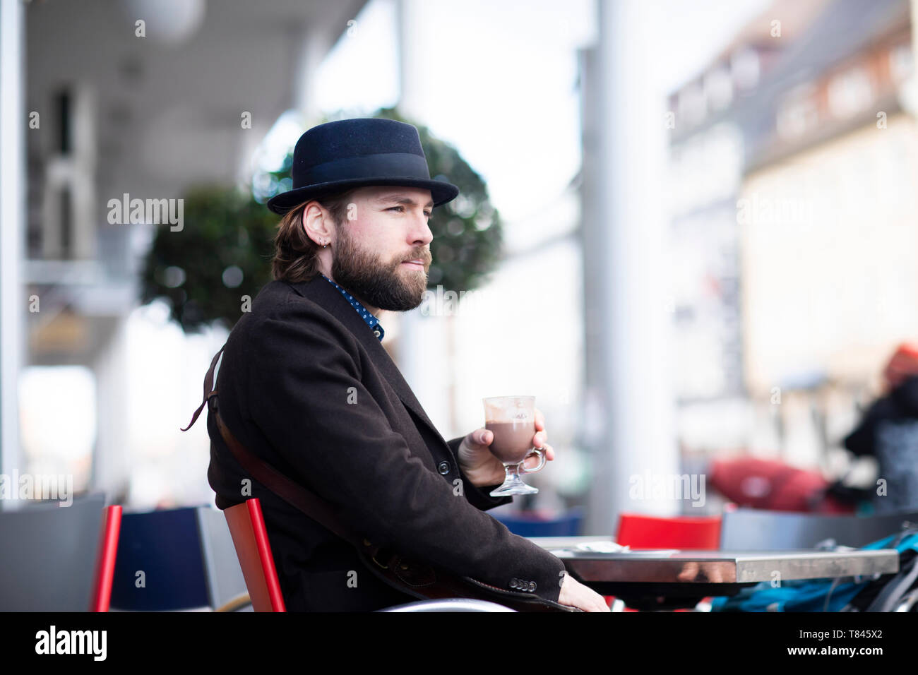 Man in trilby sitting at sidewalk cafe table Stock Photo