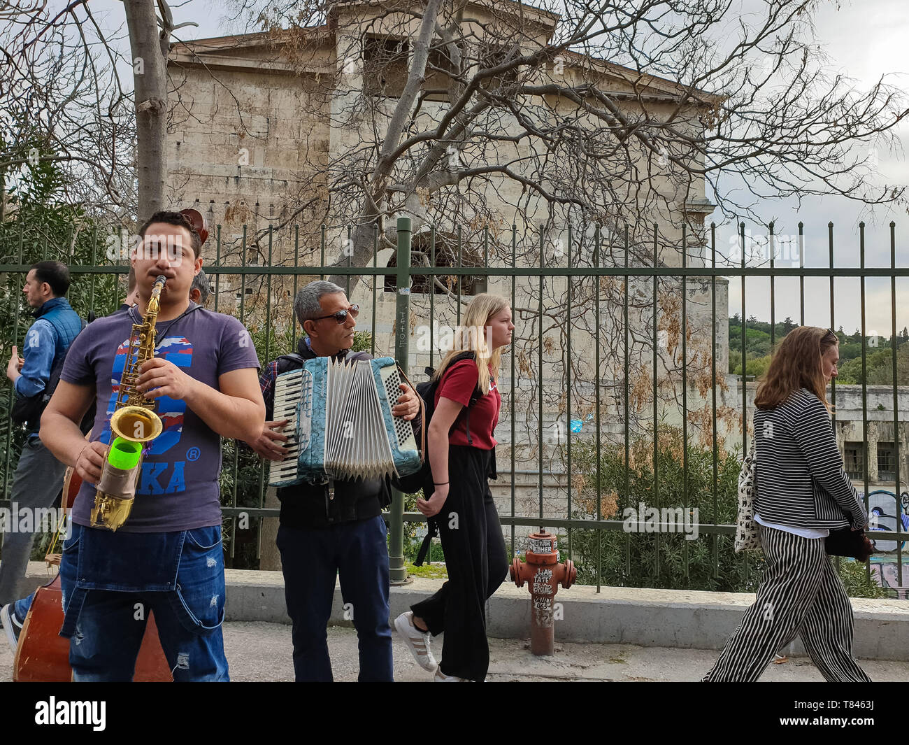 Athens, Greece - March 9, 2019: Street musicians play music at Adrianou Steet in Monastiraki as tourists pass by with Stoa of Attalos monument in the  Stock Photo