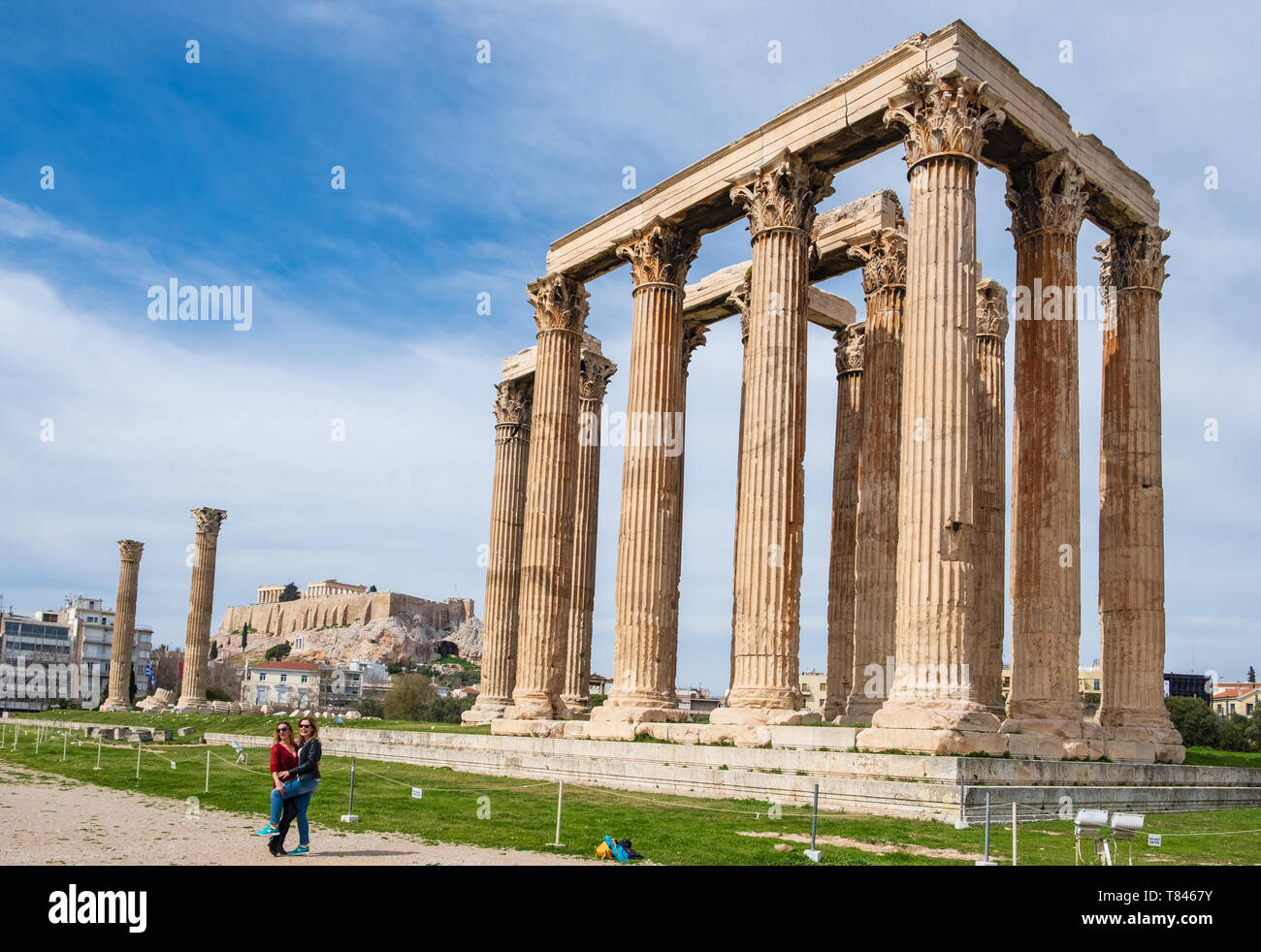 Athens, Greece - March 9, 2019: Tourists being photographed in front of the Greek Temple of Olympian Zeus with the Acropolis of Athens in the backgrou Stock Photo