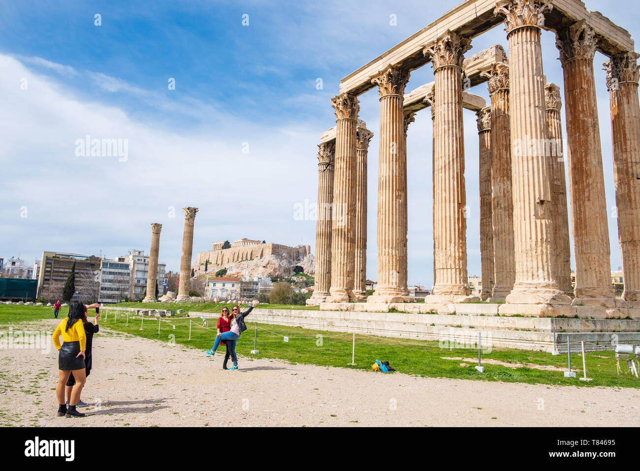 Athens, Greece - March 9, 2019: Tourists being photographed in front of the Greek Temple of Olympian Zeus with the Acropolis of Athens in the backgrou Stock Photo