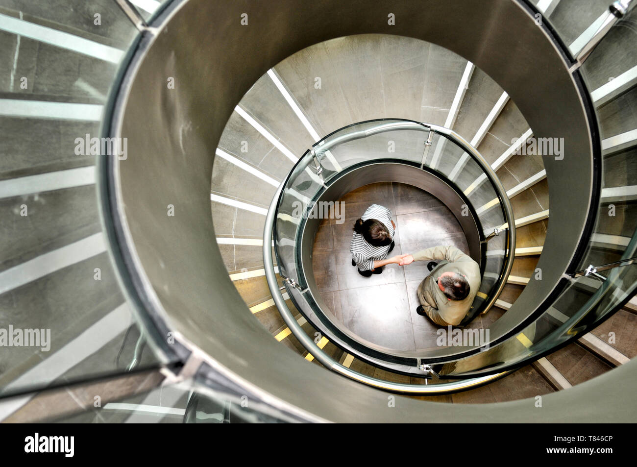 Businessman and businesswoman shaking hands below spiral staircase Stock Photo