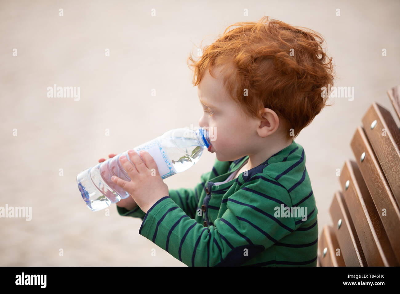 Boy drinking water on park bench Stock Photo